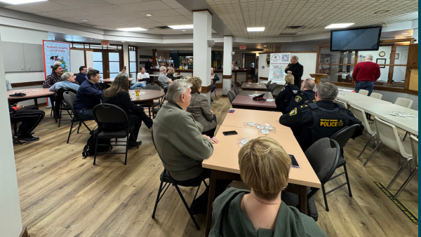 Large room of people sitting at tables listening to a speaker