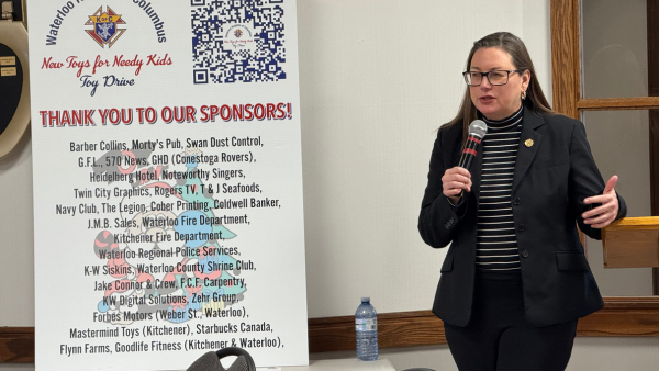 Woman in suit jacket with long dark hair and glasses talking into a microphone