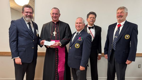 Men in suits with a bishop handing him a cheque