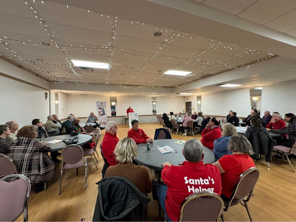 Picture of a large room with people sitting at round tables listening to a speaker