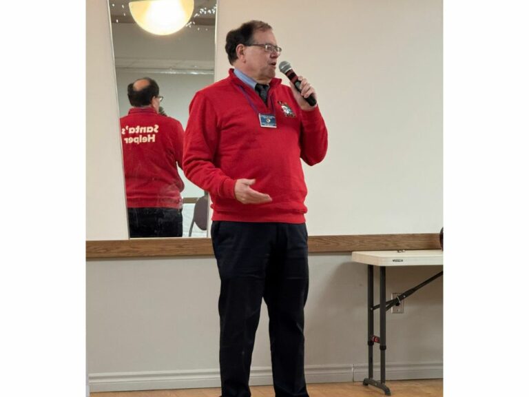 Man in red sweatshirt in front of a room speaking on a microphone
